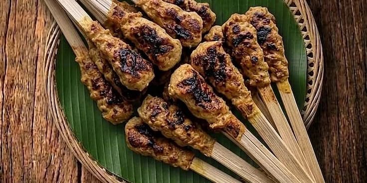 Sate lilit Bali — daging berbumbu kelapa dililitkan pada batang bambu, dibakar di atas arang, disajikan di atas daun pisang dalam tampah bambu